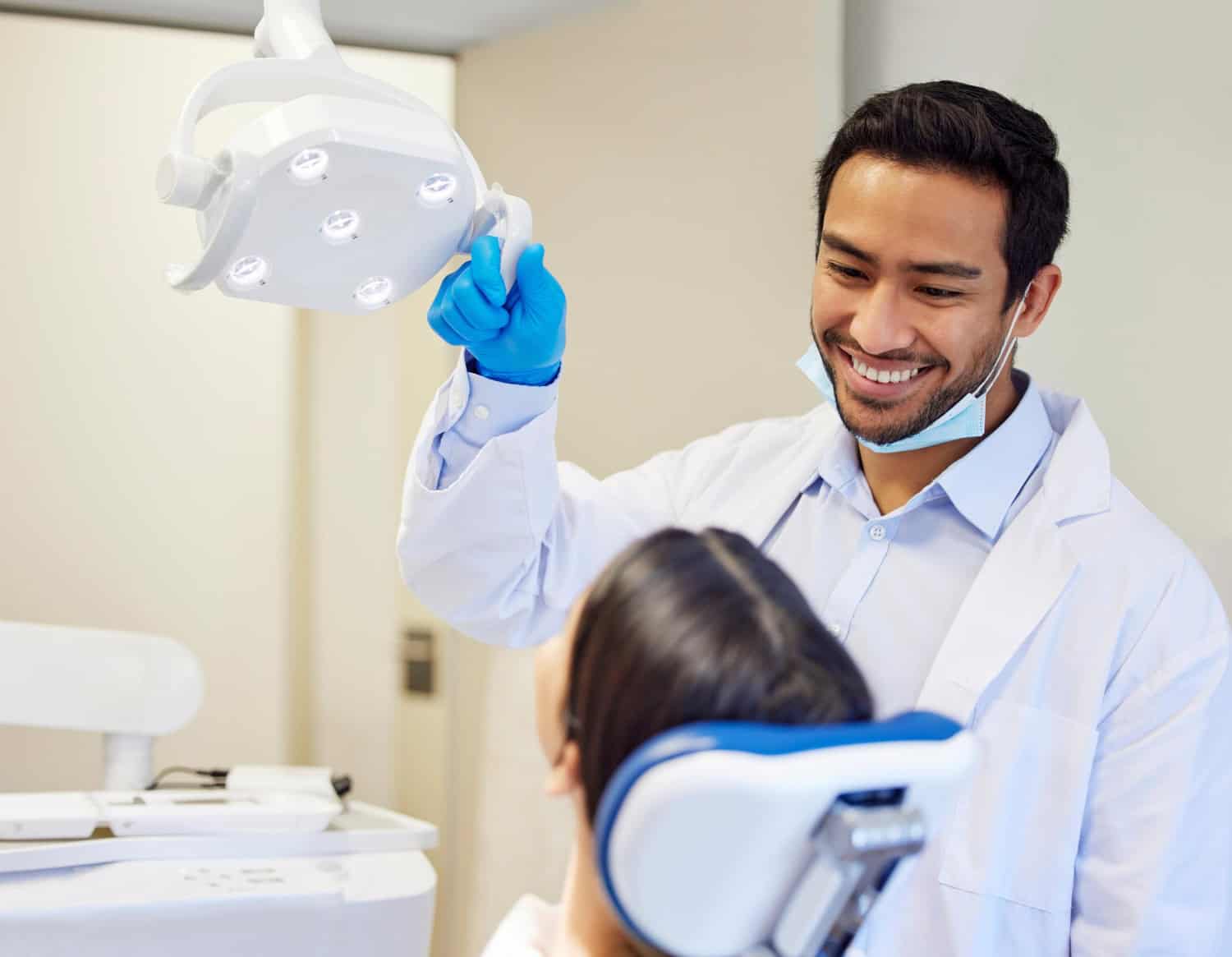 Dentist adjusting the dental exam light while preparing a patient for a professional teeth whitening consultation and exam.