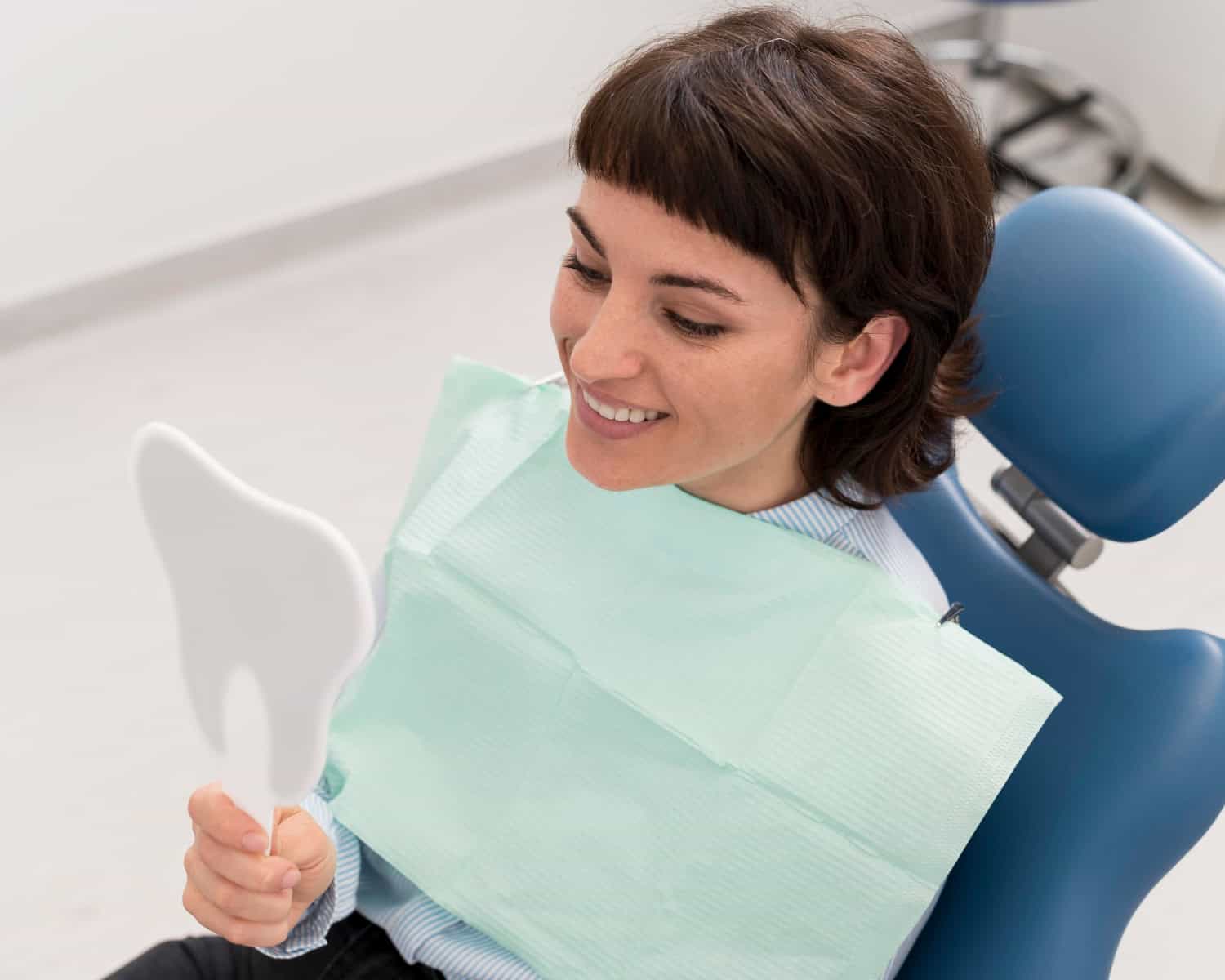 Dental patient smiling while examining her teeth in a handheld mirror during a cosmetic dentistry visit.